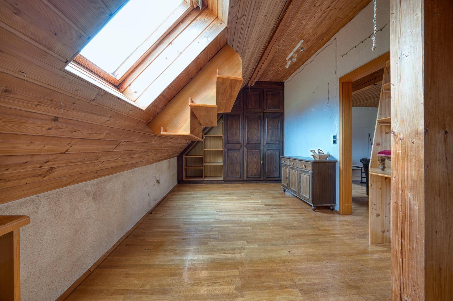 Dachzimmer mit Holzverkleidung, Holzboden und großem Dachfenster, ideal für ein Kinderzimmer.