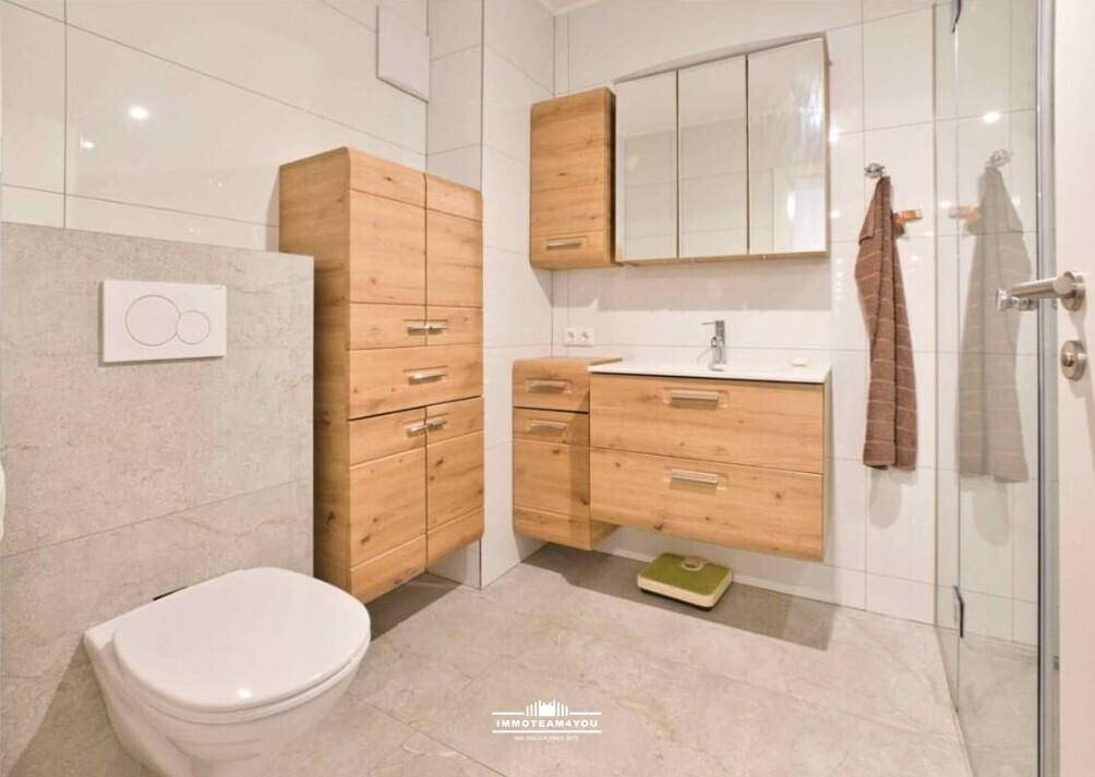 Modernes Badezimmer mit hellgrauen Fliesen, Holzmöbeln und wandhängendem WC.