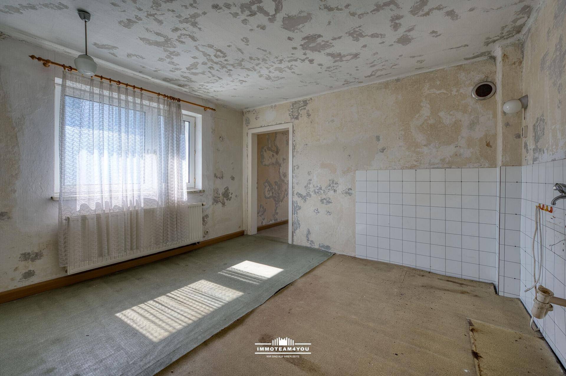 Renovierungsbedürftiger Raum mit Fenster, Fliesenbereich und abgenutztem Bodenbelag.