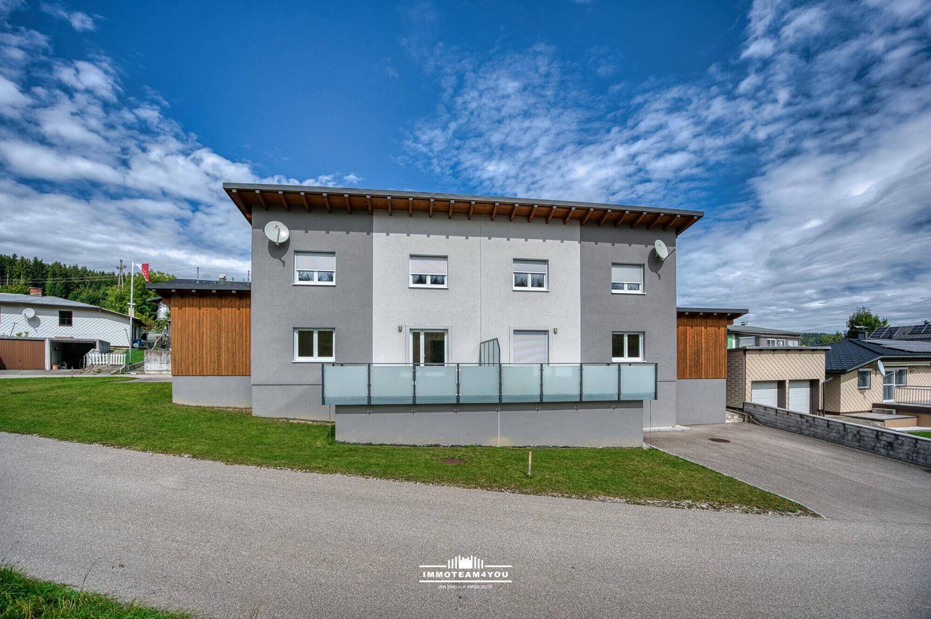 Rückansicht des modernen Hauses mit Terrasse, Glasgeländer und gepflegtem Rasen.