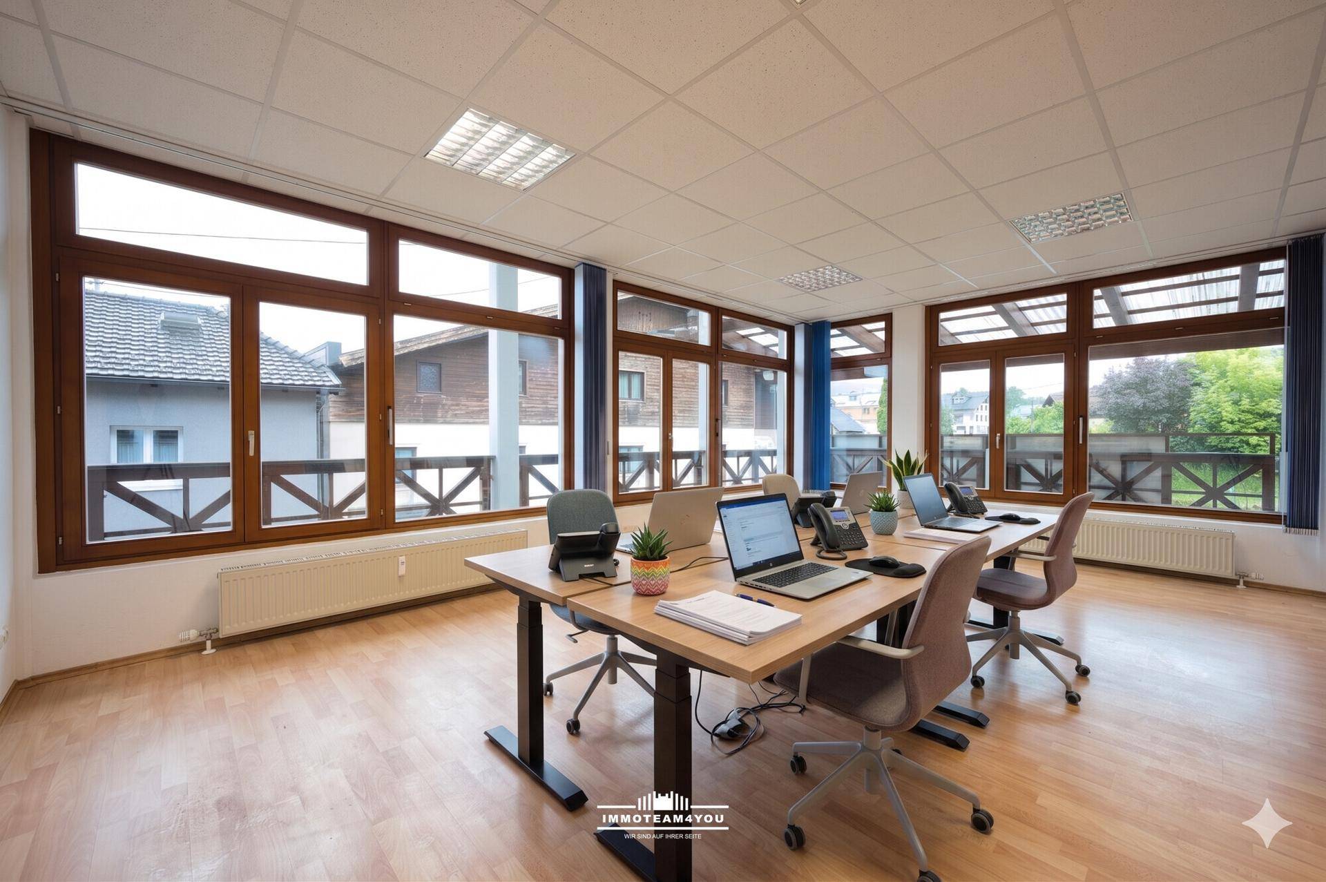 Helles und modernes Büro mit mehreren Arbeitsplätzen, großen Fenstern und Laminatboden.