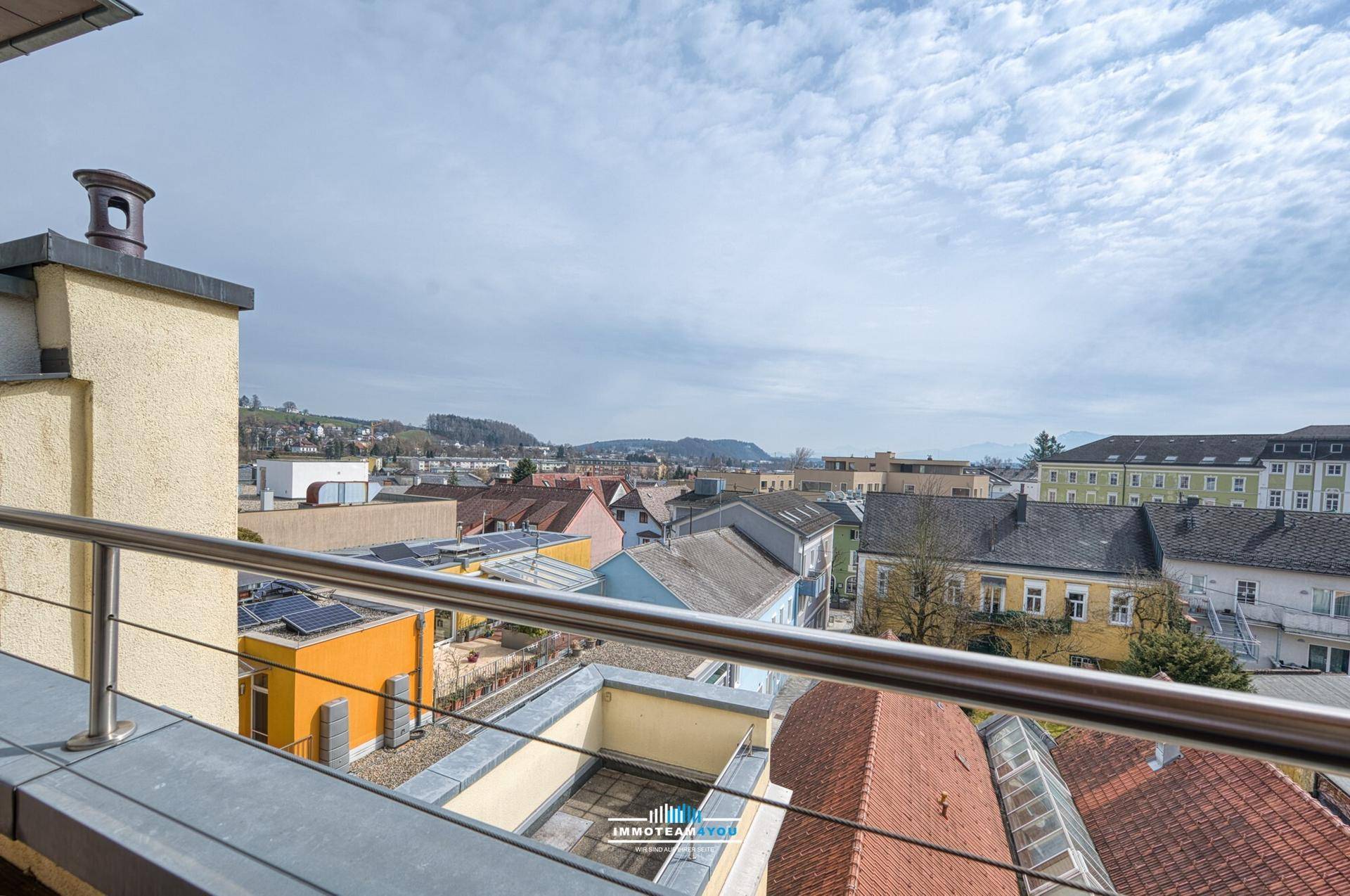 Balkon mit Edelstahlgeländer und weitem Blick über die Dächer der Stadt und die Landschaft.