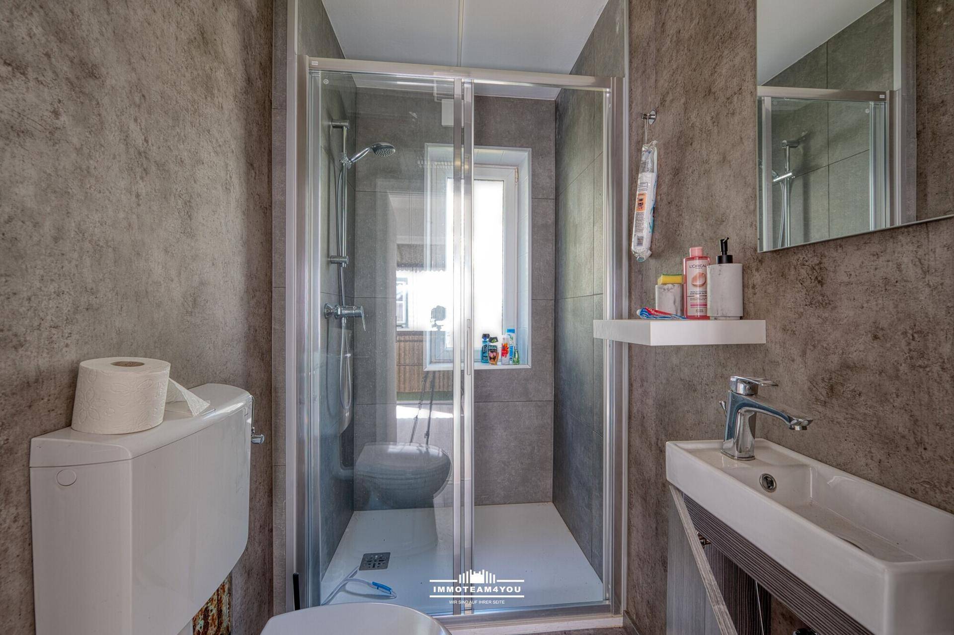 Modernes Badezimmer mit Duschkabine, Wand-WC und kleinem Waschbecken in Grautönen.