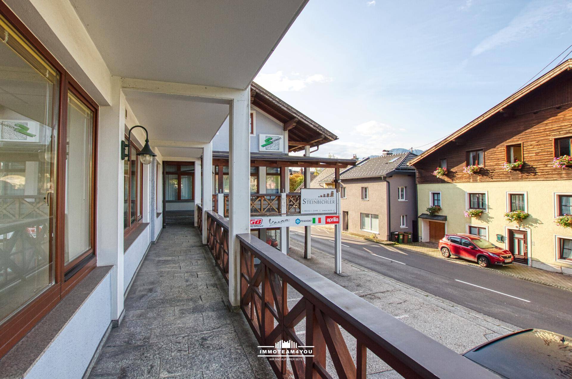 Langer, überdachter Balkon mit Blick auf die Straße und die umliegenden Gebäude der Nachbarschaft.