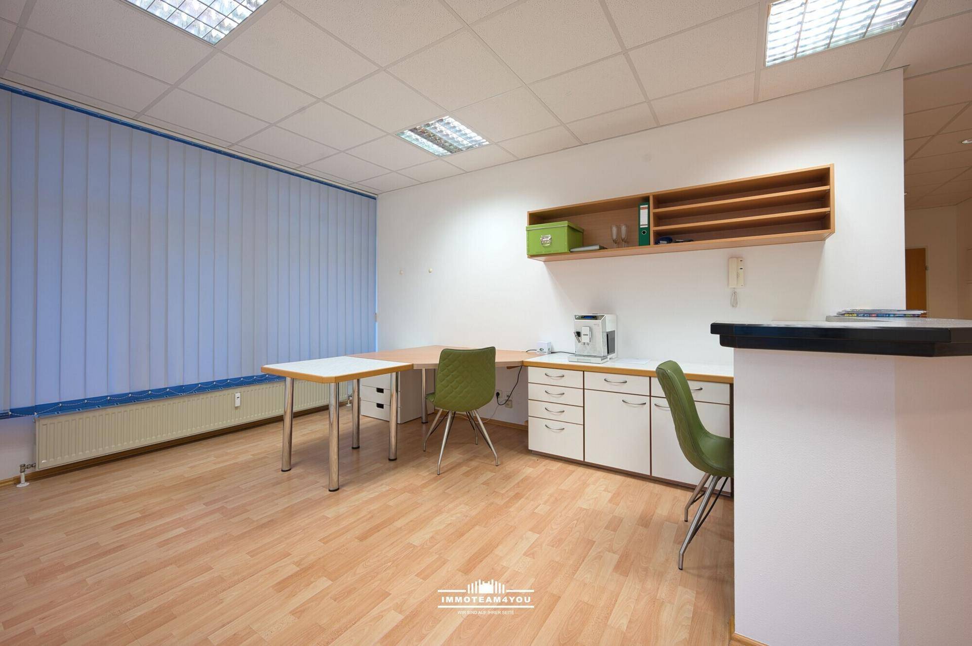 Heller Bürobereich mit Holzboden, Schreibtisch und einer kleinen Küchenzeile oder Kaffeestation.