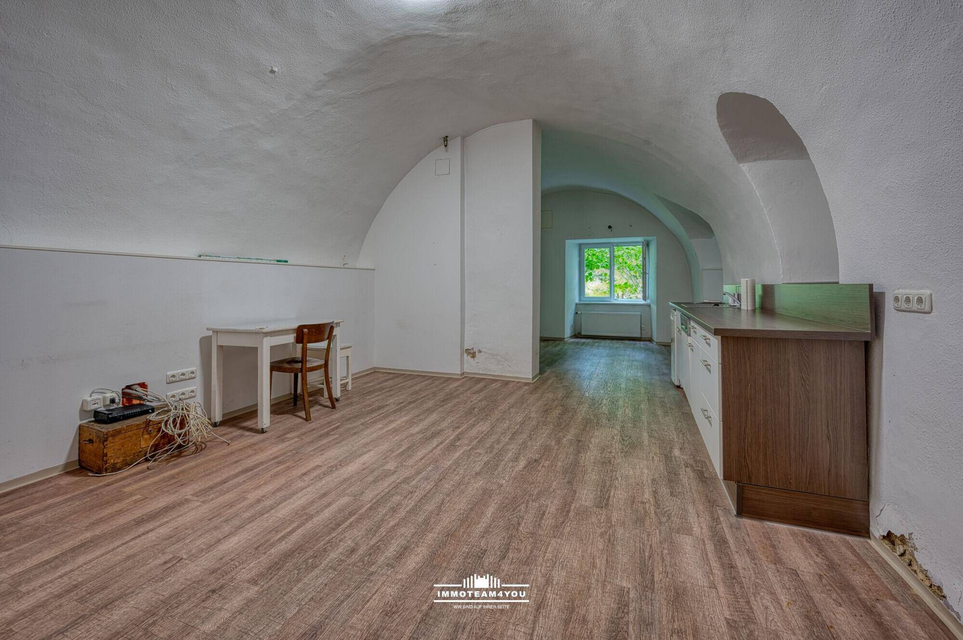 Geräumiger Wohnbereich mit Gewölbedecke, Laminatboden und einem Fenster mit Blick ins Grüne.