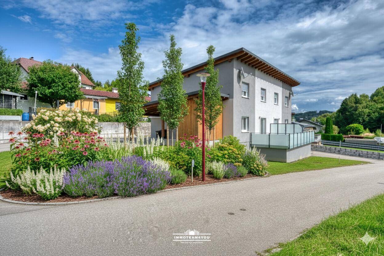 Modernes Haus mit ansprechend gestaltetem Vorgarten, blühenden Pflanzen und jungen Bäumen.