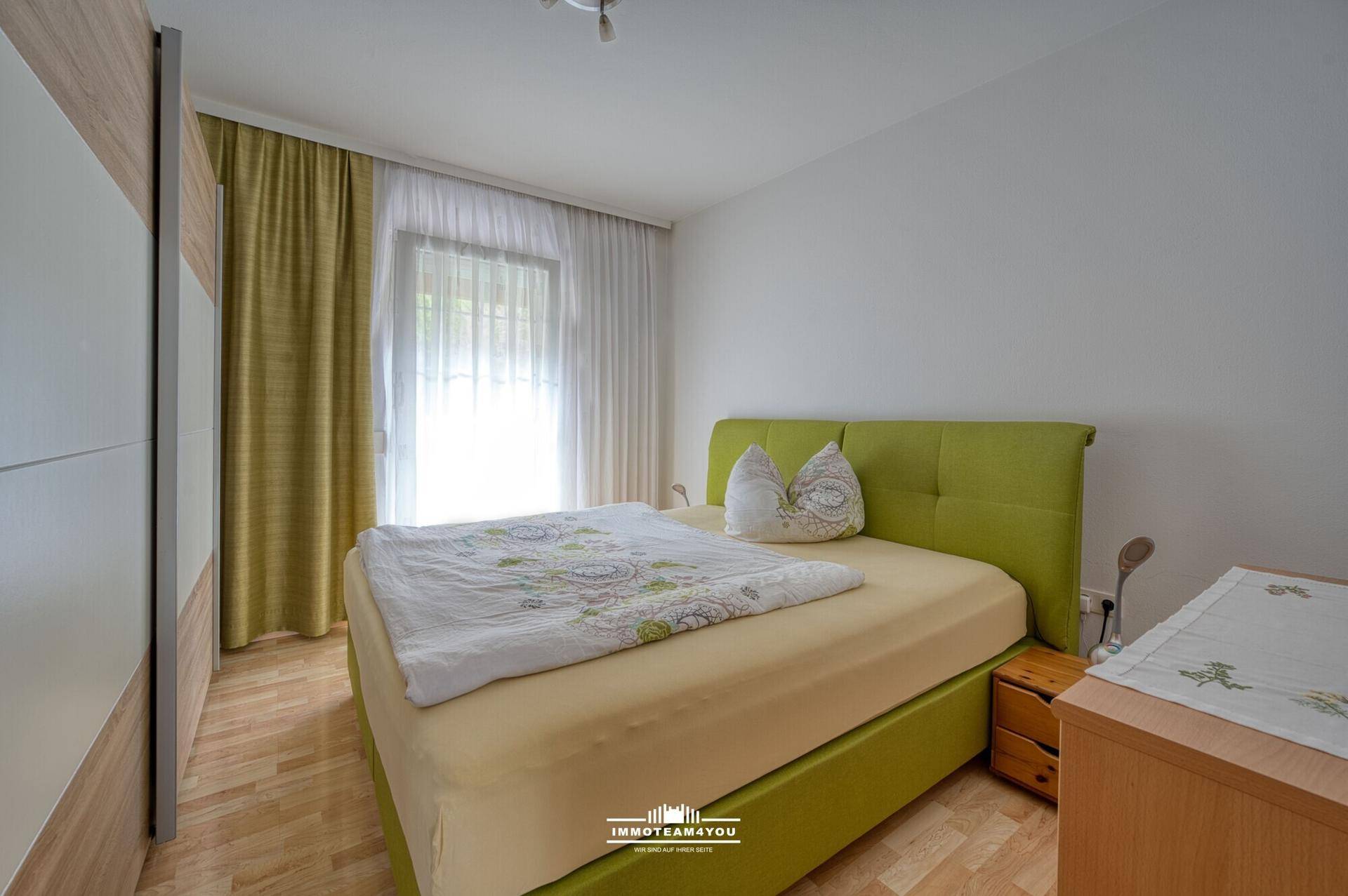 Schlafzimmer mit hellem Holzboden, großem Bett und Zugang zu einem Außenbereich.