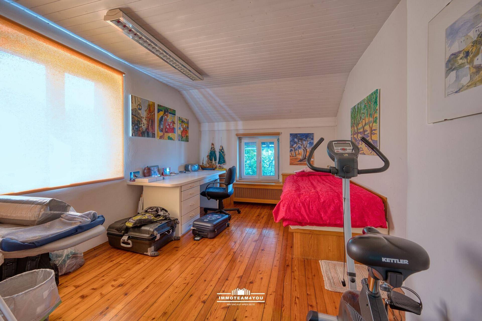 Geräumiges Schlafzimmer mit Holzboden, Dachschrägen und einem Arbeitsbereich mit Schreibtisch.