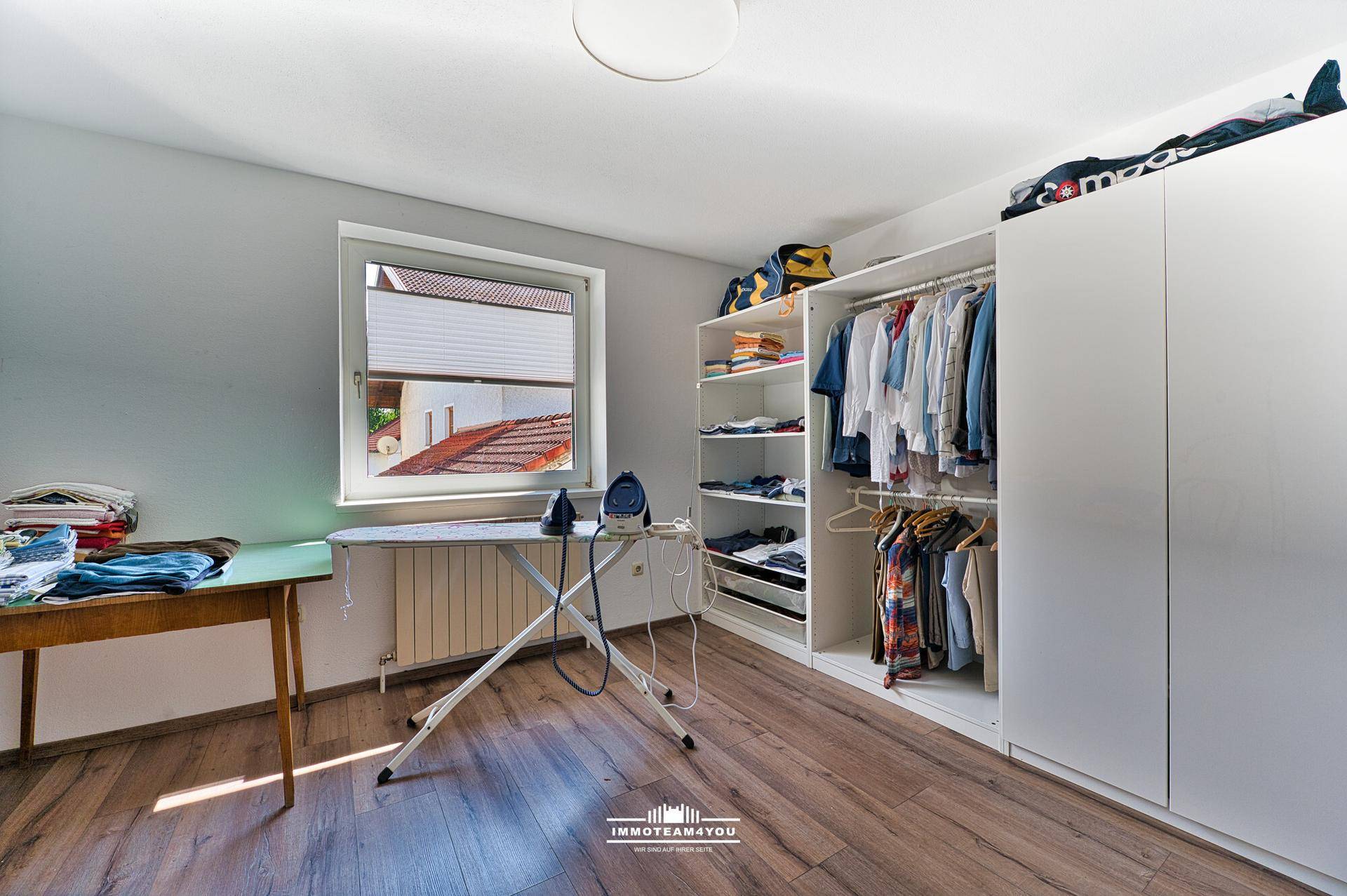 Praktischer Hauswirtschaftsraum mit Laminatboden, Fenster und offenem Kleiderschrank.