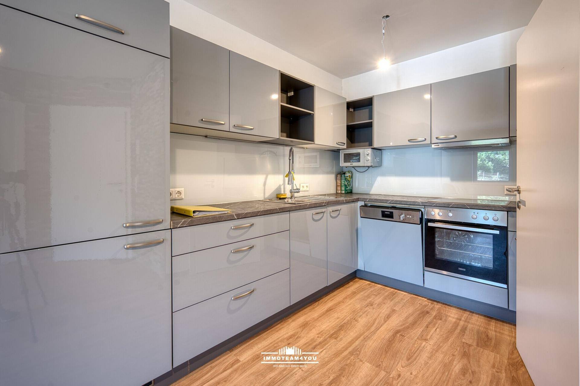 Moderne Küche mit grauen Hochglanzschränken, Einbaugeräten und Laminatboden.