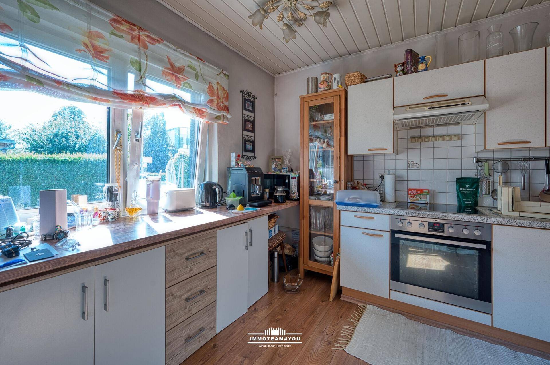 Helle Küche mit Einbauschränken, Holztheke und großem Fenster mit Blick ins Grüne.