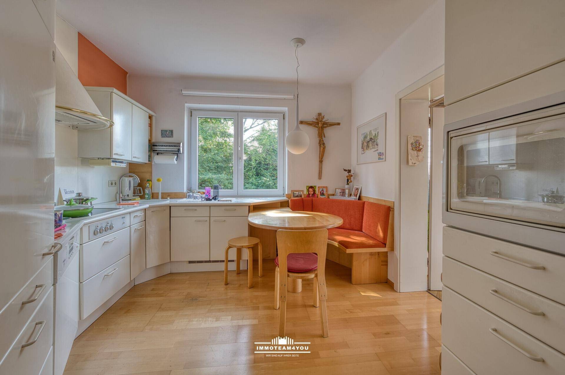 Helle Einbauküche mit Essecke, Holzmöbeln und Fenster mit Blick ins Grüne.