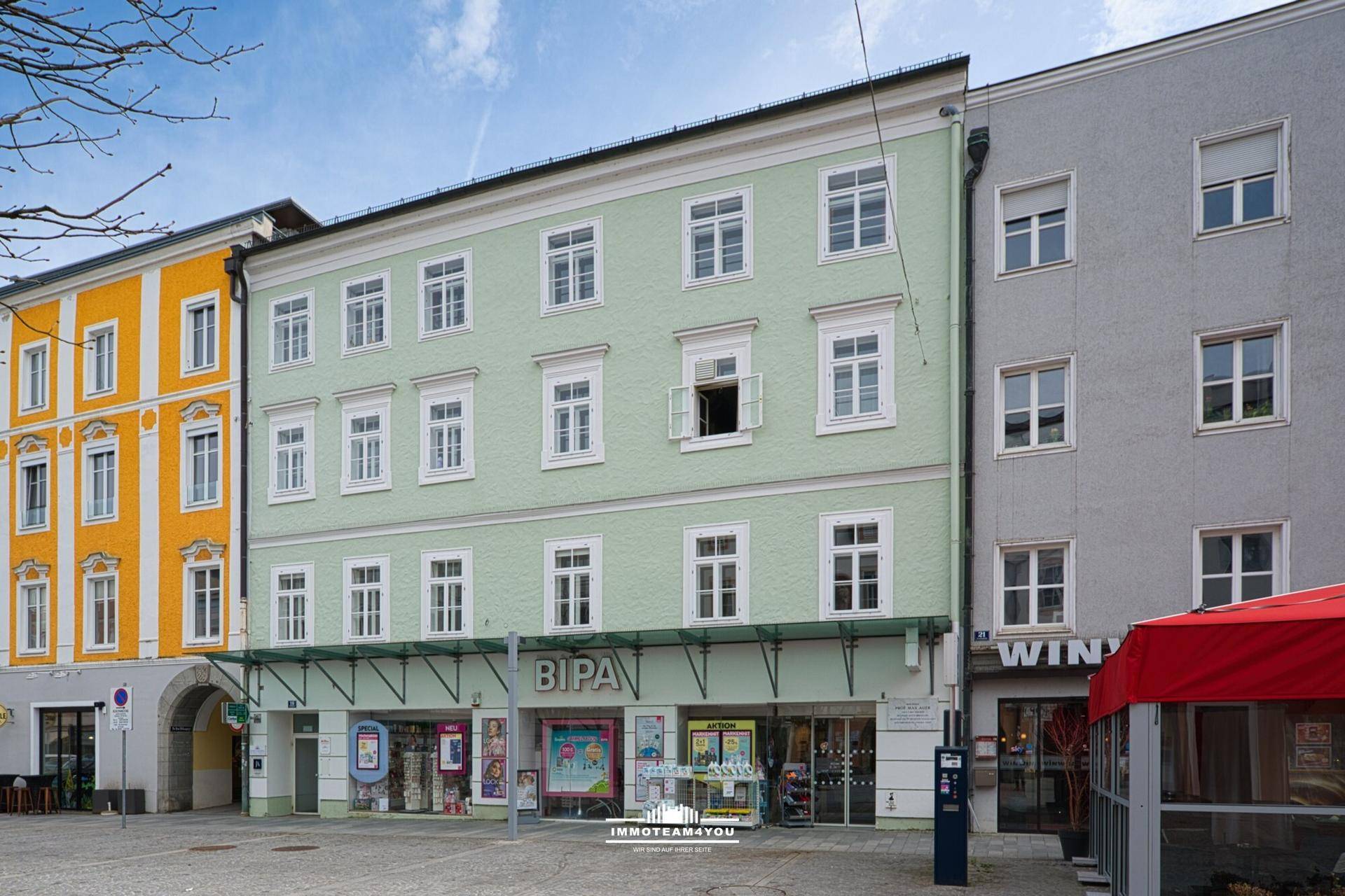 Historisches Gebäude mit hellgrüner Fassade und Geschäften im Erdgeschoss an einem sonnigen Tag.