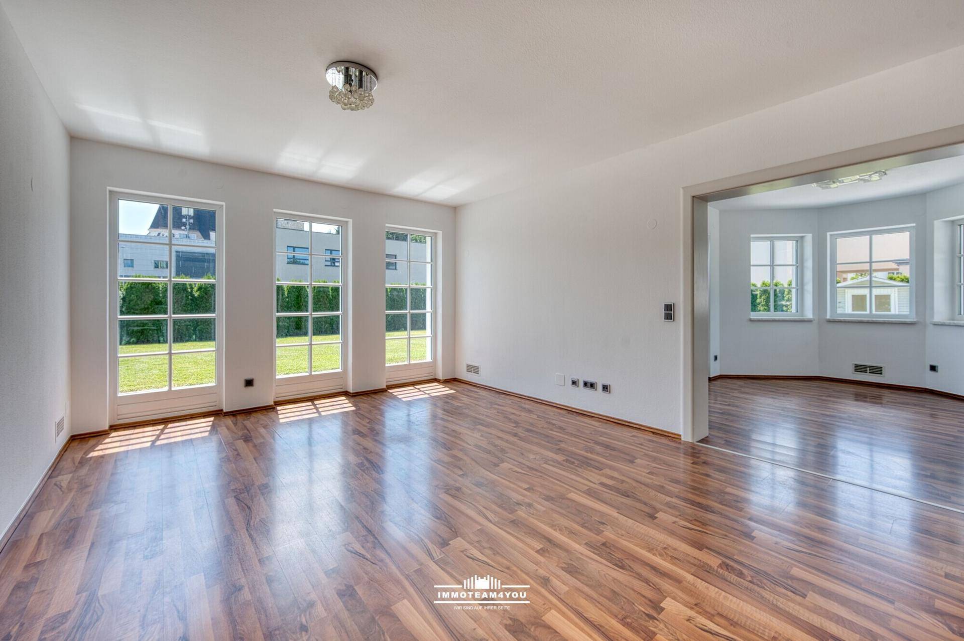 Helles Wohnzimmer mit Laminatboden und großen Fenstern zum Garten.
