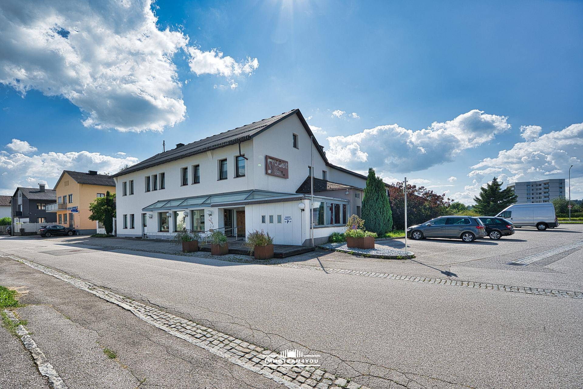 Außenansicht eines Gebäudes mit großzügigen Fenstern und Parkplätzen unter blauem Himmel.