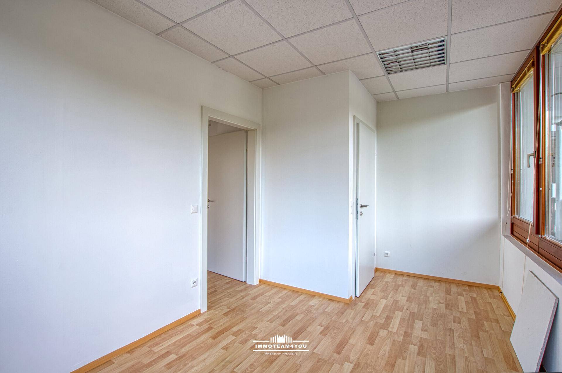 Leerer Büroraum mit Laminatboden, weißen Wänden und zwei Türen, die zu weiteren Räumen führen.