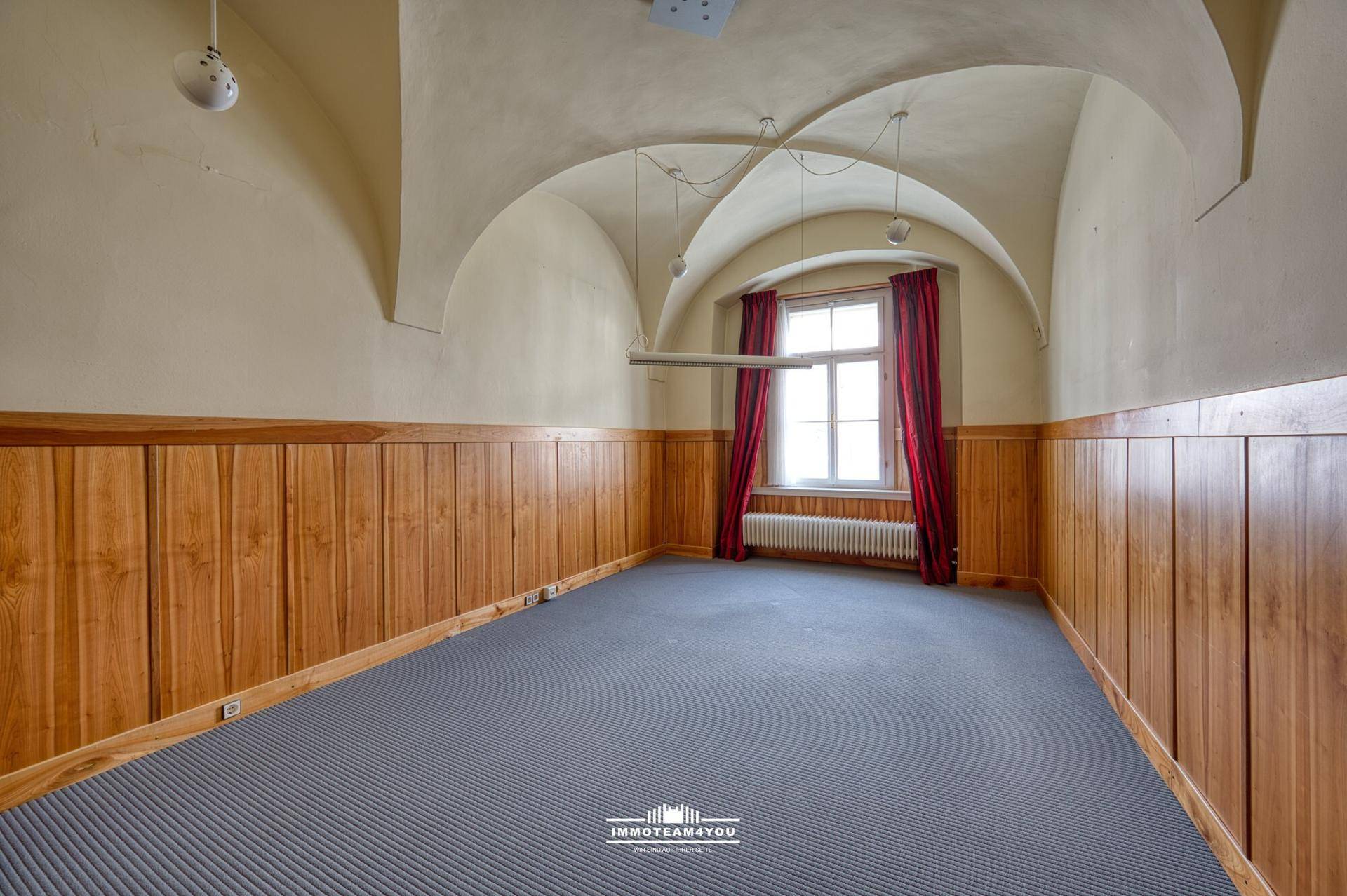 Leerer Büroraum mit Gewölbedecke, Holzvertäfelung und grauem Teppichboden, bereit zur individuellen Einrichtung.