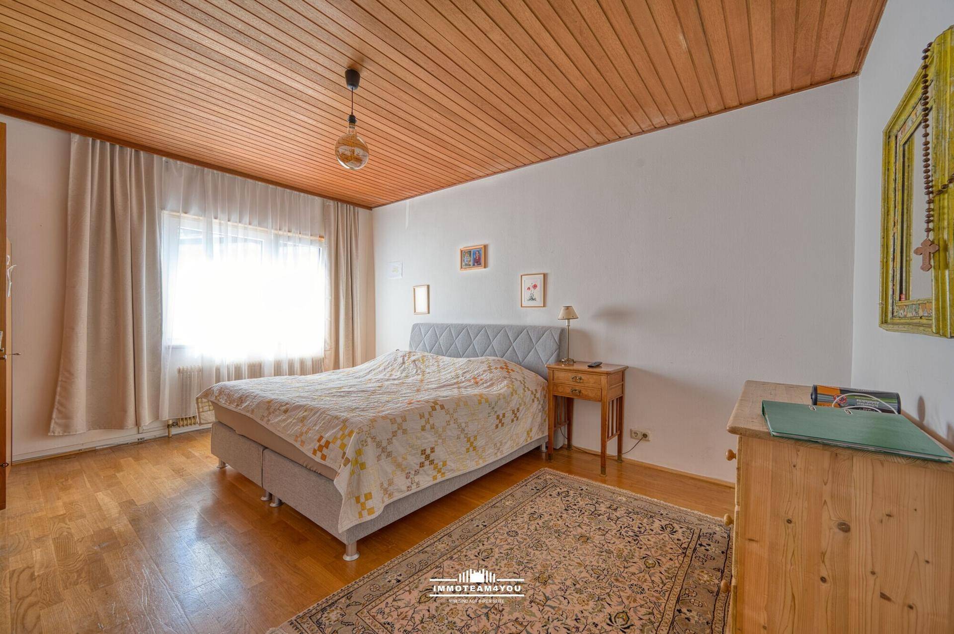 Helles Schlafzimmer mit Doppelbett, Holzdecke und einem traditionellen Teppich auf Parkettboden.