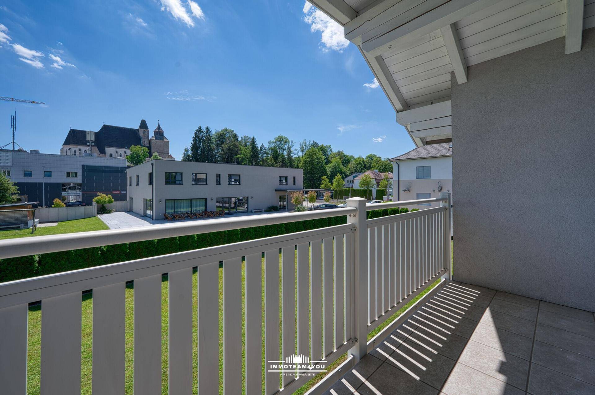 Balkon mit weißem Geländer und Blick auf die Umgebung mit einer Kirche im Hintergrund.