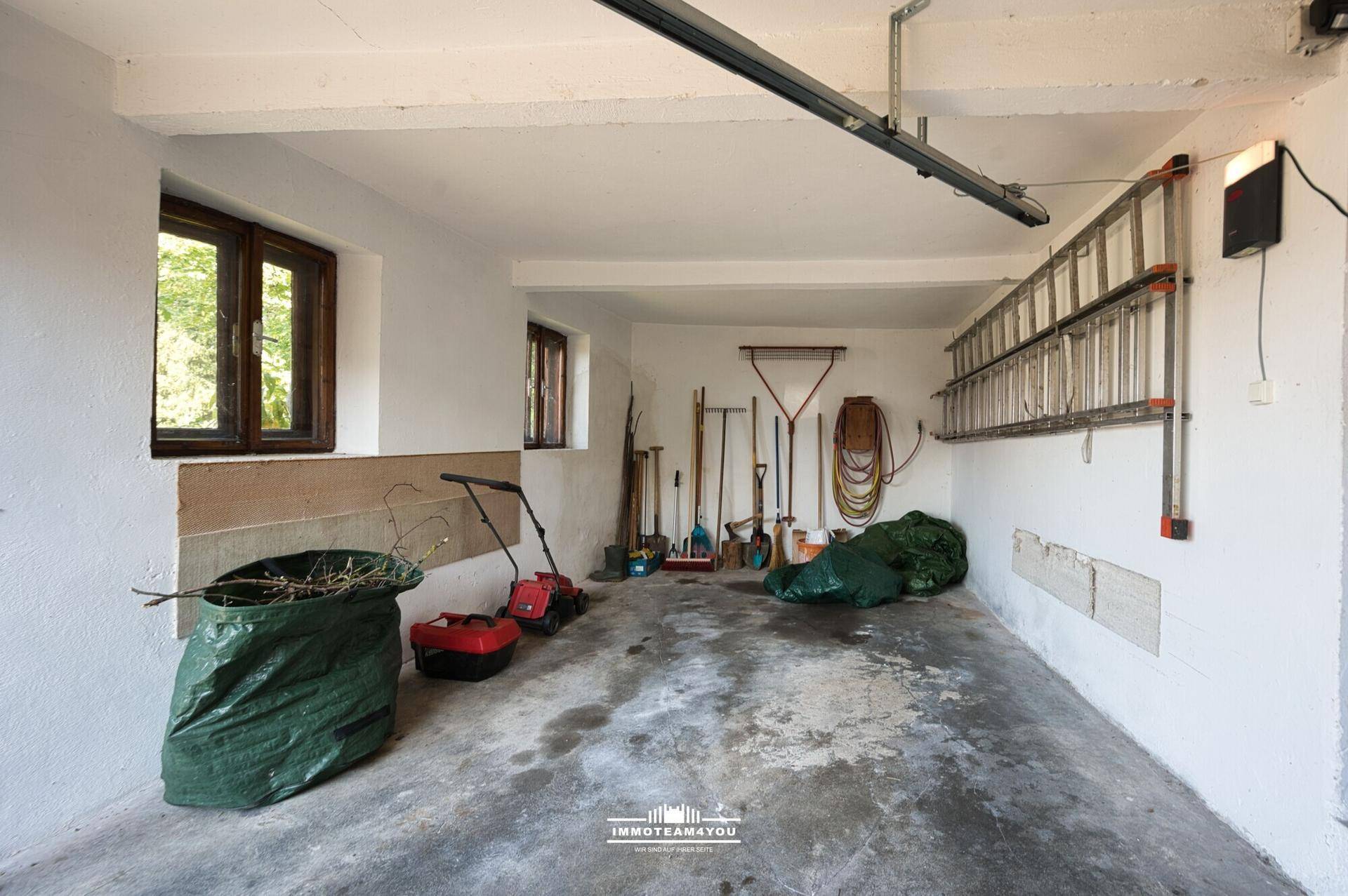 Geräumige Garage mit Betonboden, Fenstern und Stauraum für Gartengeräte.