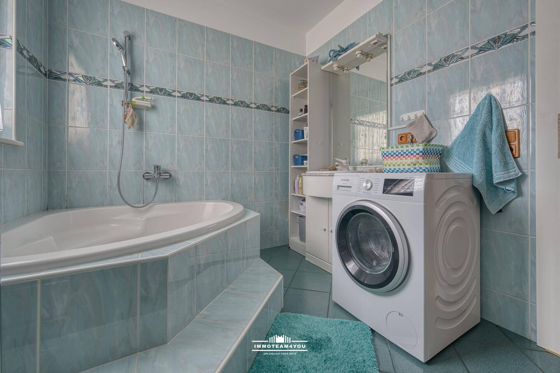 Badezimmer mit Eckbadewanne, blauen Fliesen und Waschmaschine.