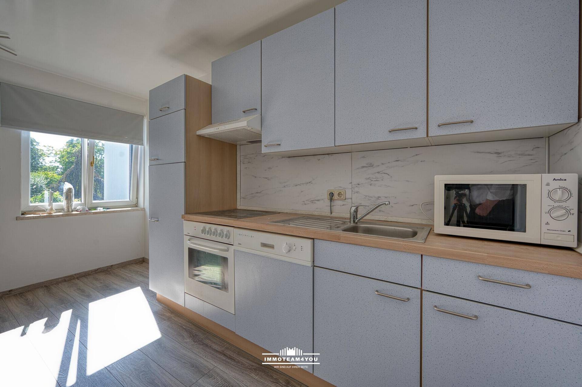 Funktionale Küche mit hellblauen Schränken, Holztheke und Blick ins Grüne durch das Fenster.