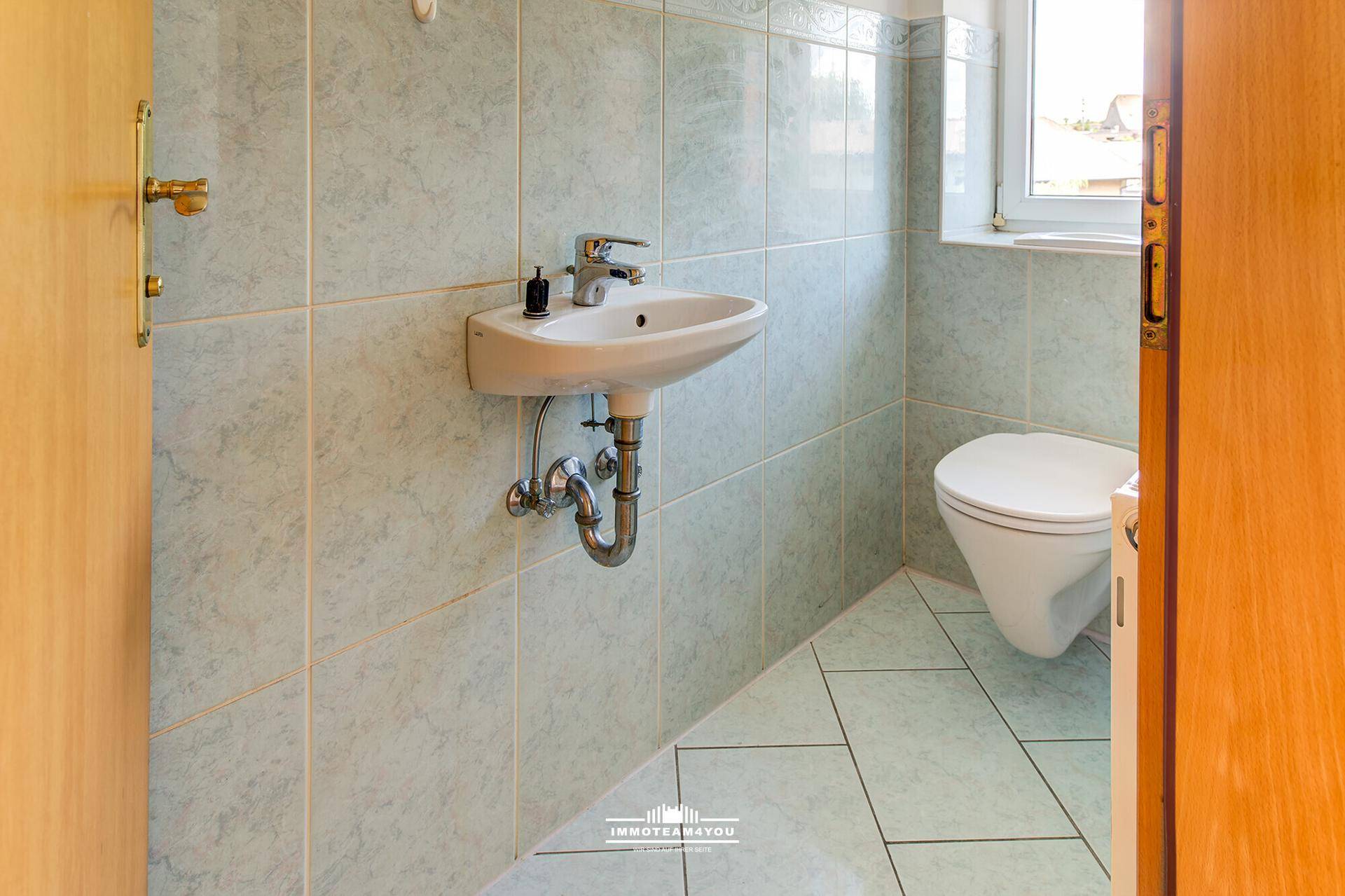 Kleines Gäste-WC mit hellblauen Fliesen, wandhängendem Waschbecken und Fenster.