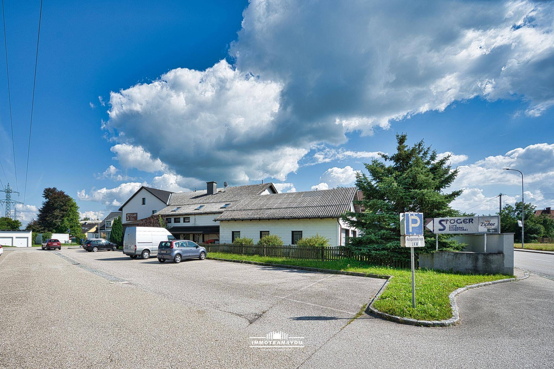Rückansicht eines Gebäudes mit Parkplatz und angrenzender Grünfläche unter blauem Himmel.
