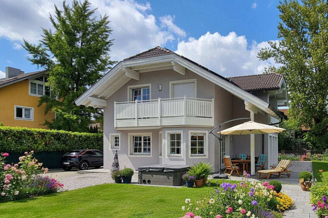 Haus mit blühendem Garten, Terrasse, Whirlpool und Sonnenschirm an einem sonnigen Tag.