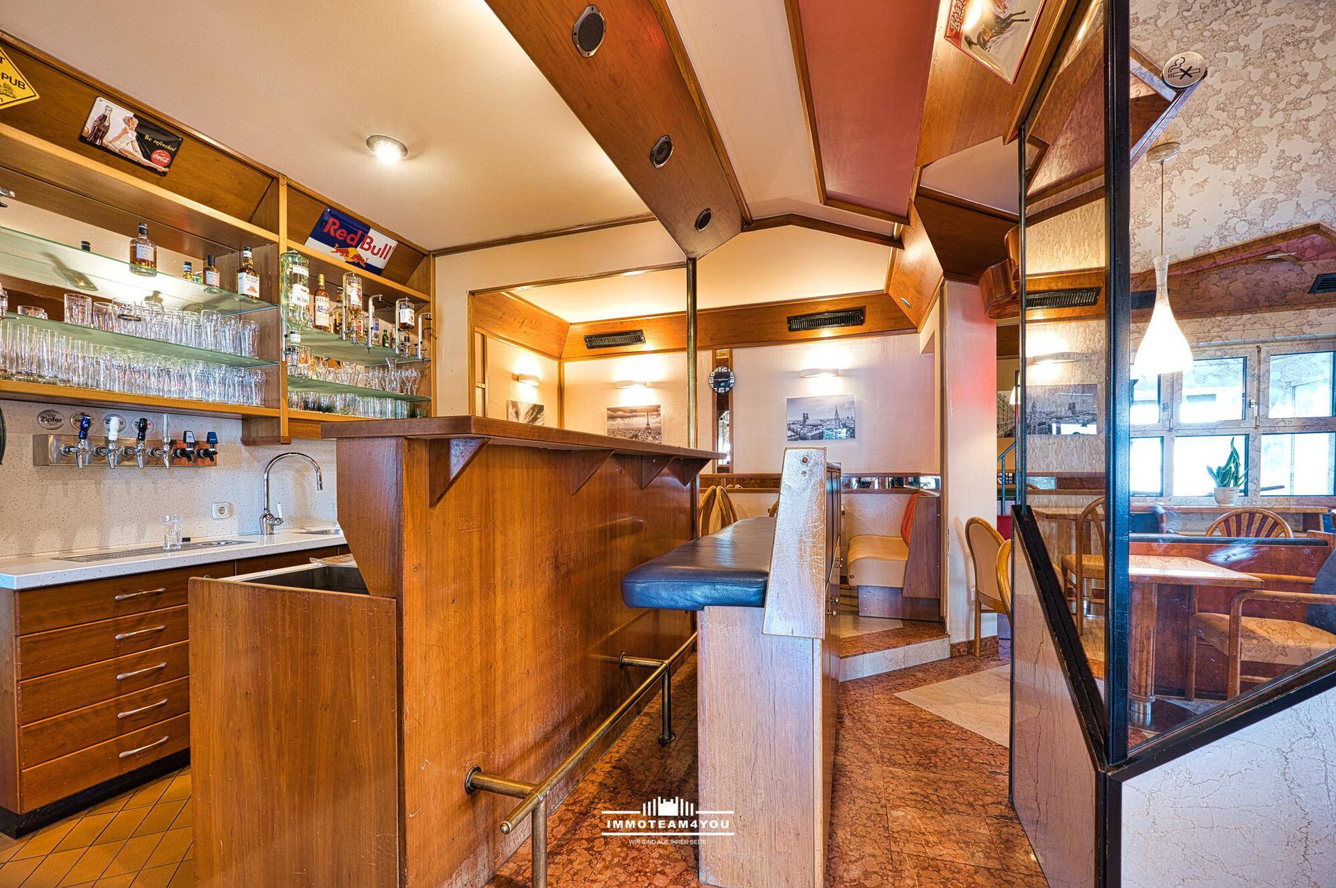 Bar mit Holztheke, Regalen voller Gläser und Flaschen sowie Sitzgelegenheiten.