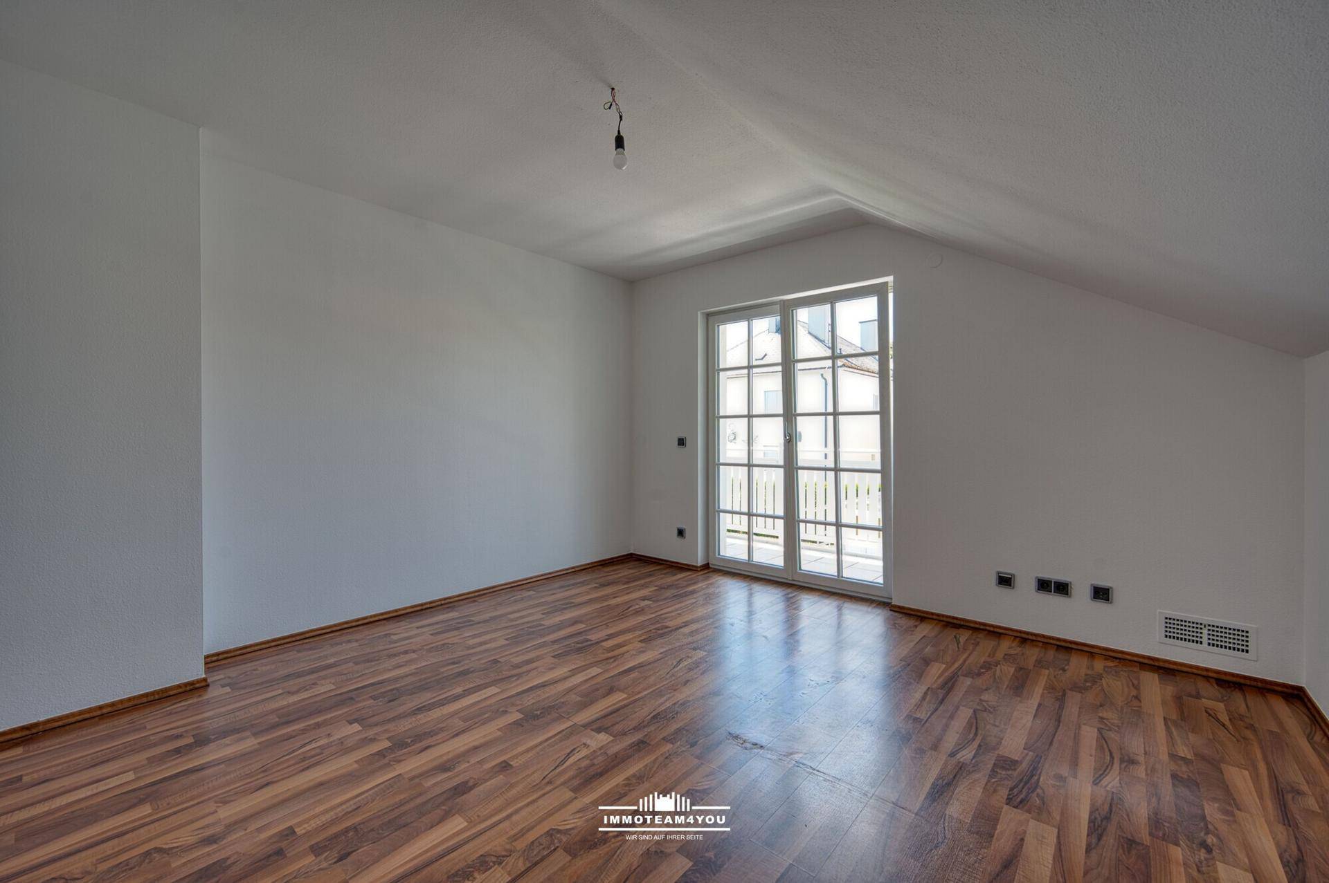 Helles Schlafzimmer im Dachgeschoss mit Laminatboden und Balkonzugang.