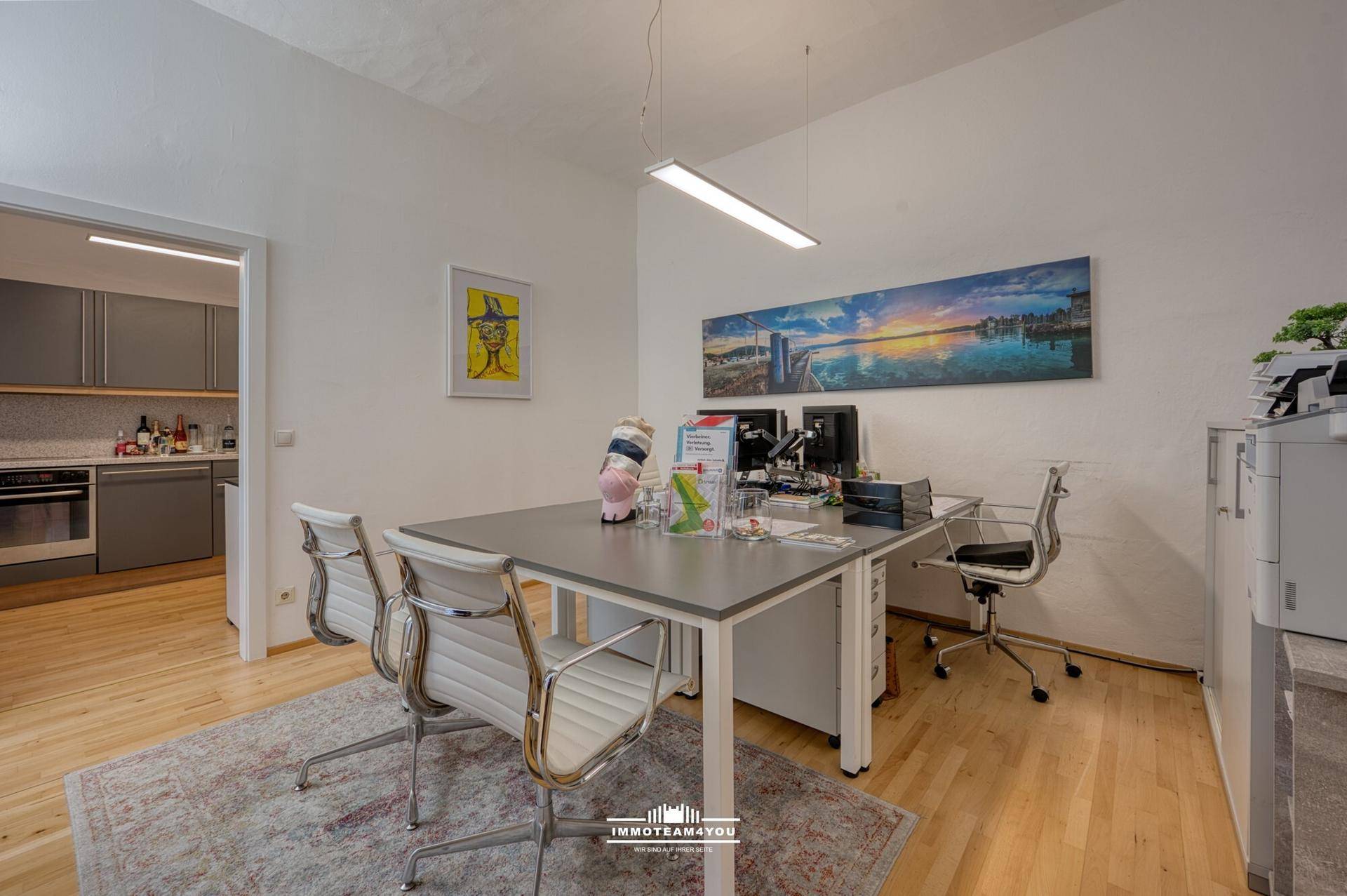 Modernes Büro mit Schreibtisch, Bürostühlen und Blick auf eine angrenzende Küche.