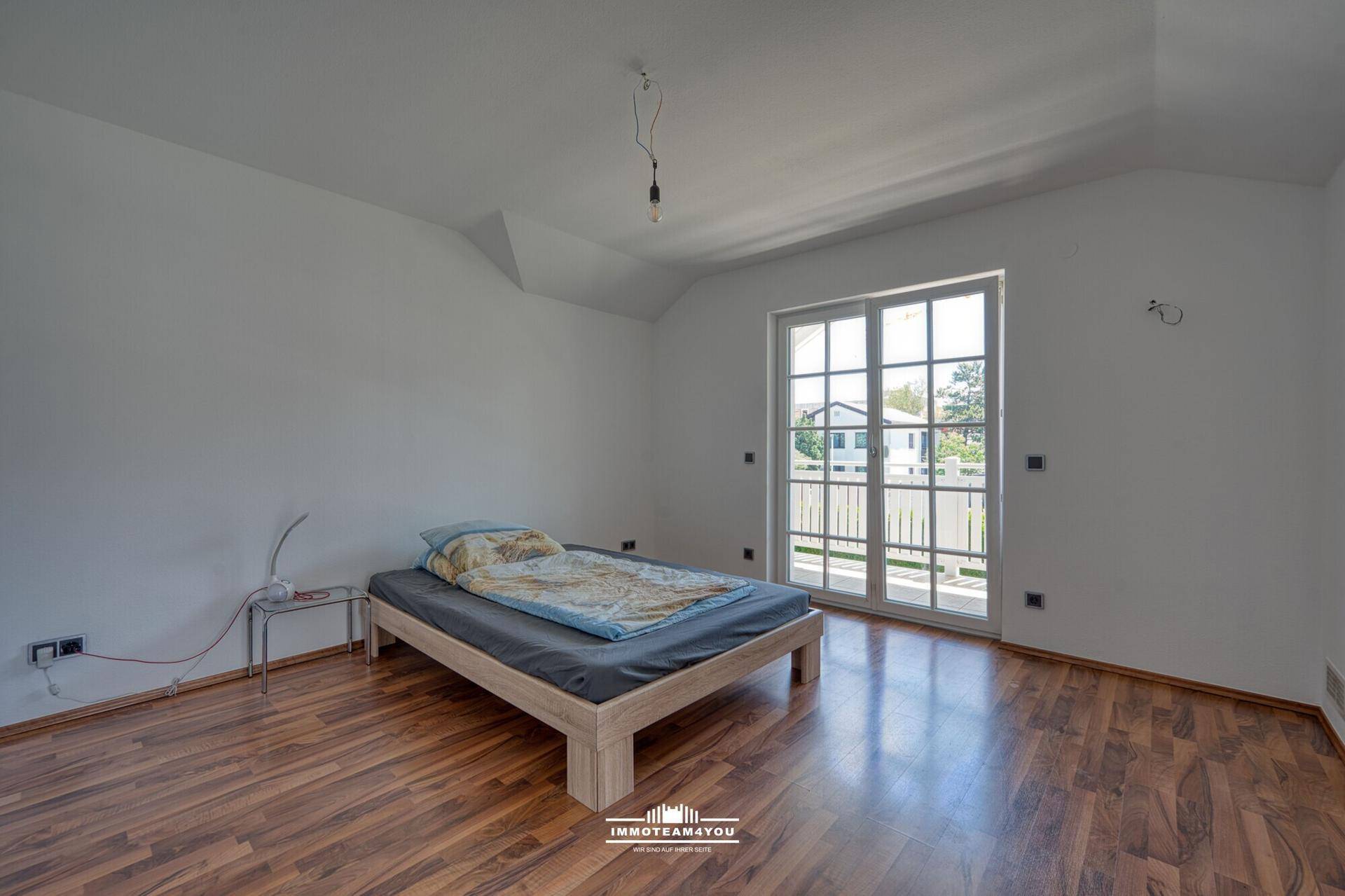 Schlafzimmer im Dachgeschoss mit Laminatboden, Bett und Balkonzugang.