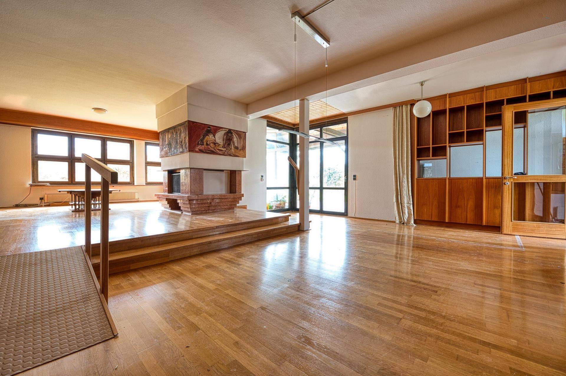 Geräumiges Wohnzimmer mit Holzboden, großem Kamin und Zugang zu einem Wintergarten.