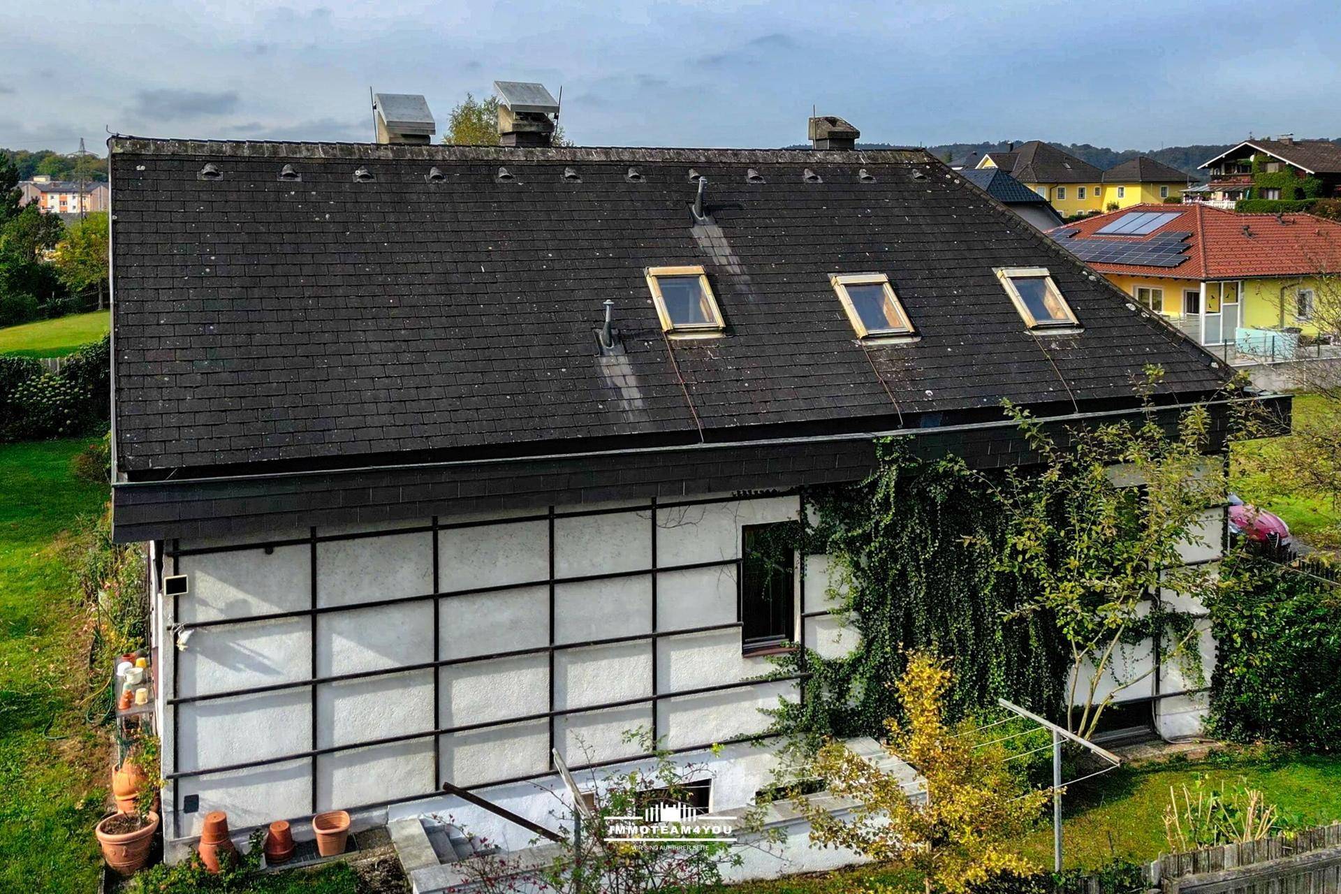 Seitenansicht des Hauses mit dunklem Dach, Dachfenstern und einem grünen Gartenbereich.