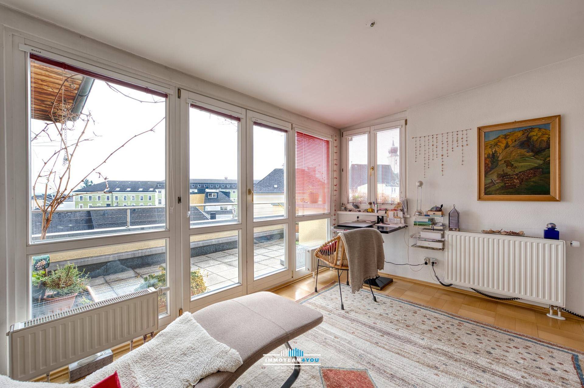 Helles Zimmer mit großen Fenstern, die auf eine Dachterrasse blicken, und einem bequemen Liegesofa.
