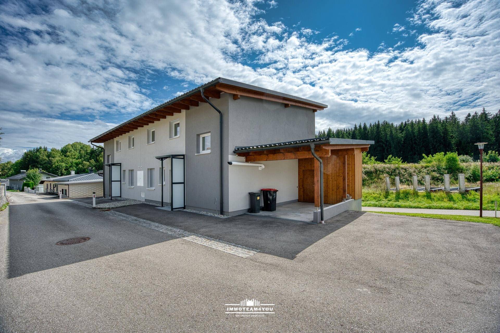 Seitenansicht des modernen Hauses mit Carport und angrenzender Straße in grüner Umgebung.