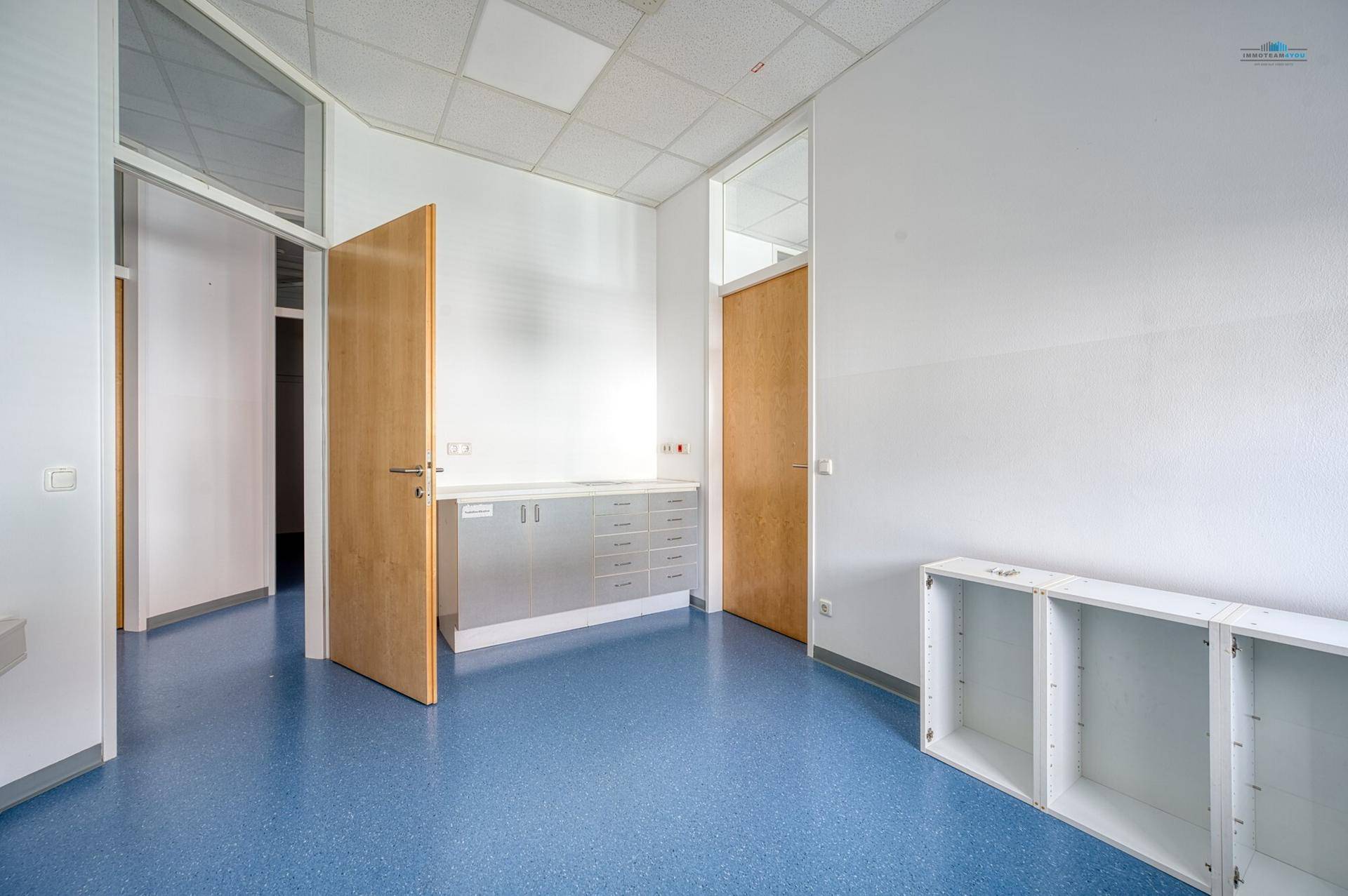 Funktionaler Gewerberaum mit blauer Bodenfläche, weißen Wänden und einer eingebauten Theke mit Metallschubladen.