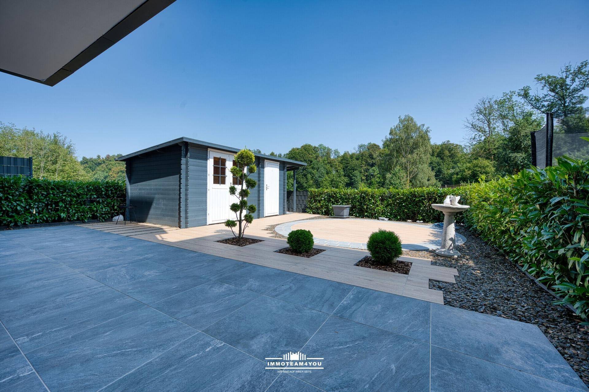 Geräumige Terrasse mit Fliesen- und Holzoptikboden, umgeben von gepflegten Hecken.