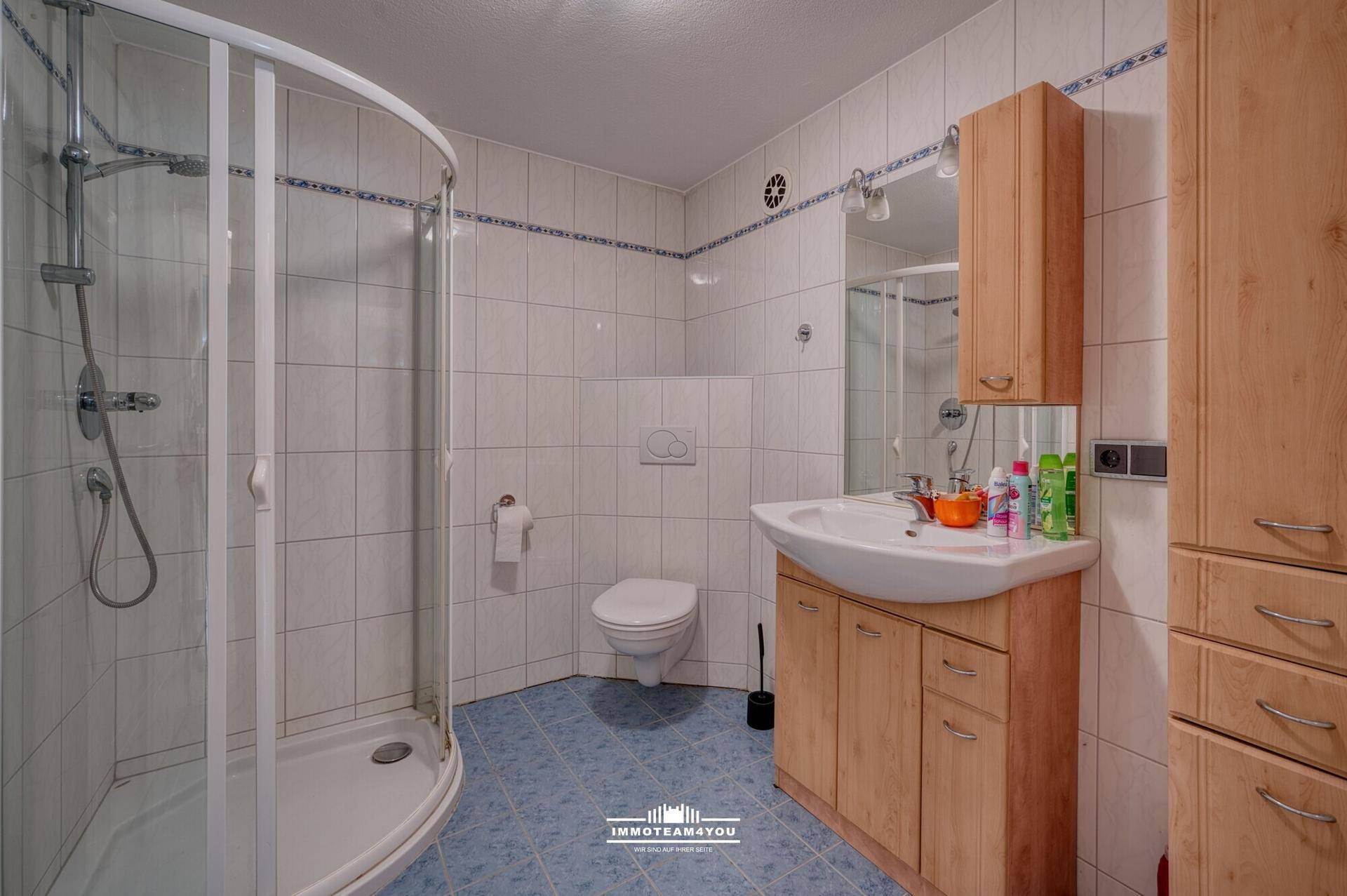 Badezimmer mit Dusche, WC, Waschbecken und Holzschränken.