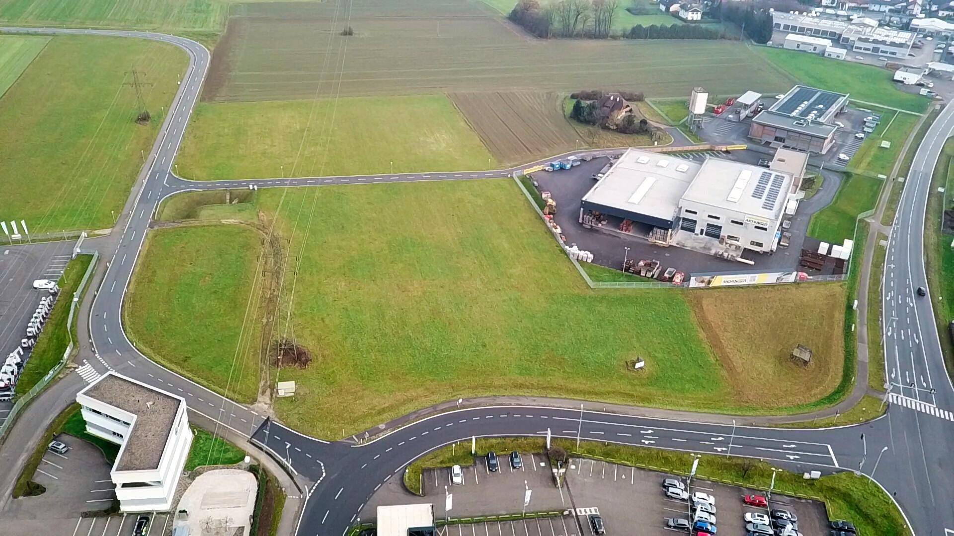 Weitläufige Luftaufnahme eines unbebauten Grundstücks umgeben von Straßen und Gewerbegebäuden unter einem grauen Himmel.