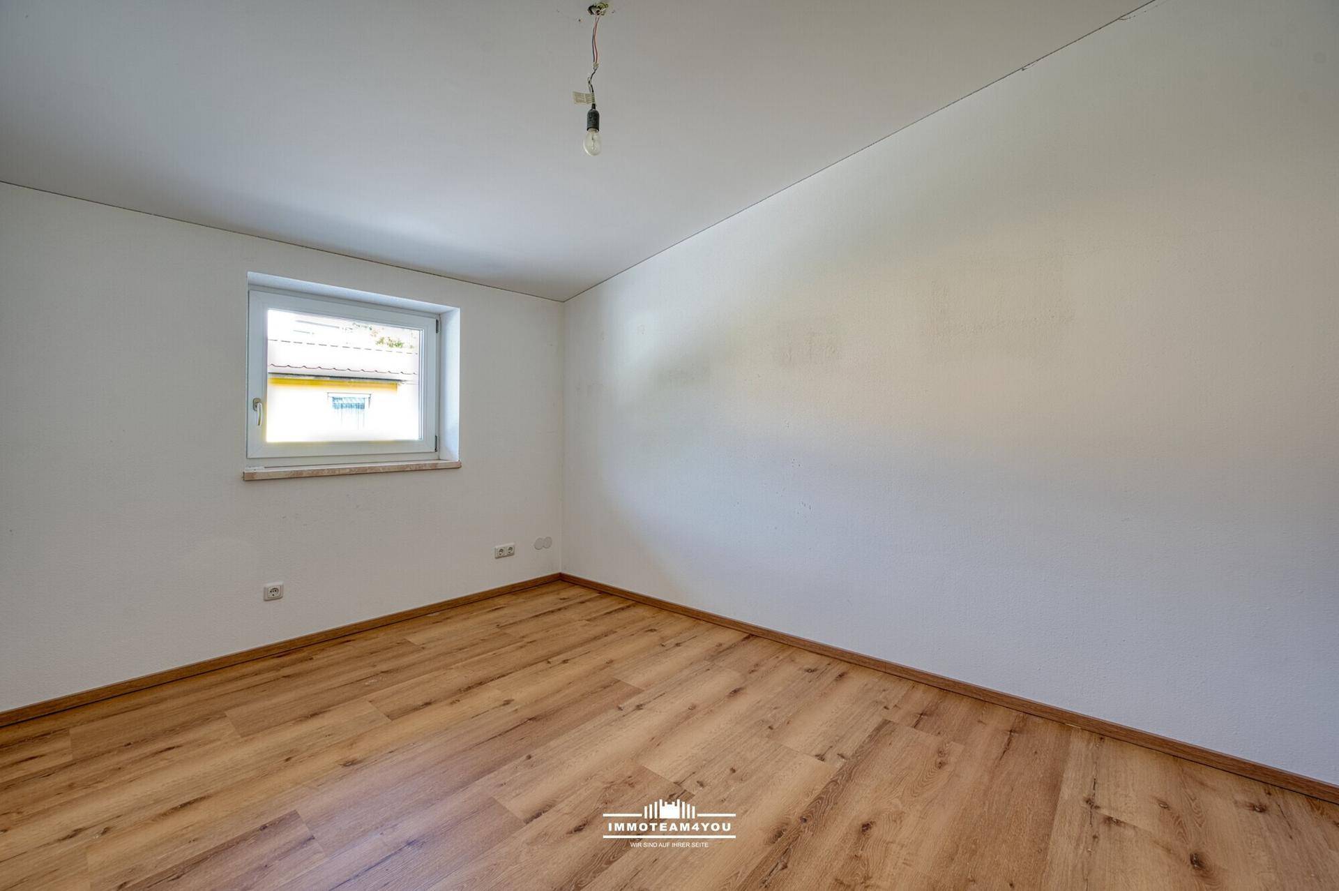 Leeres Schlafzimmer mit Holzboden, weißen Wänden und Fenster mit Blick auf die Nachbarschaft.