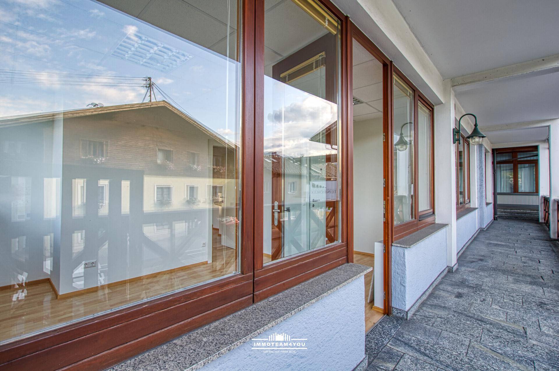 Überdachter Balkon mit Holzgeländer und großen Fenstern, die den Innenraum reflektieren.