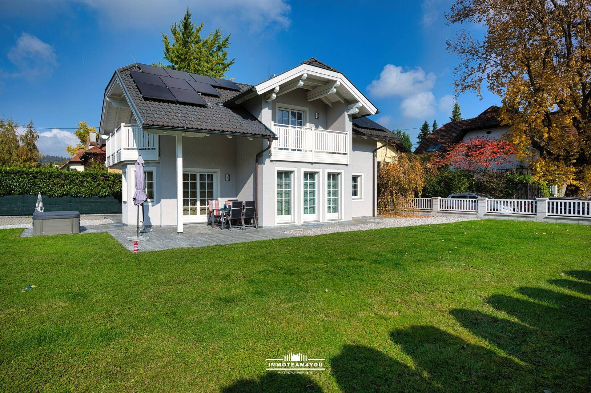 Haus mit großem Garten, Terrasse, Photovoltaikanlage und blauer Himmel.