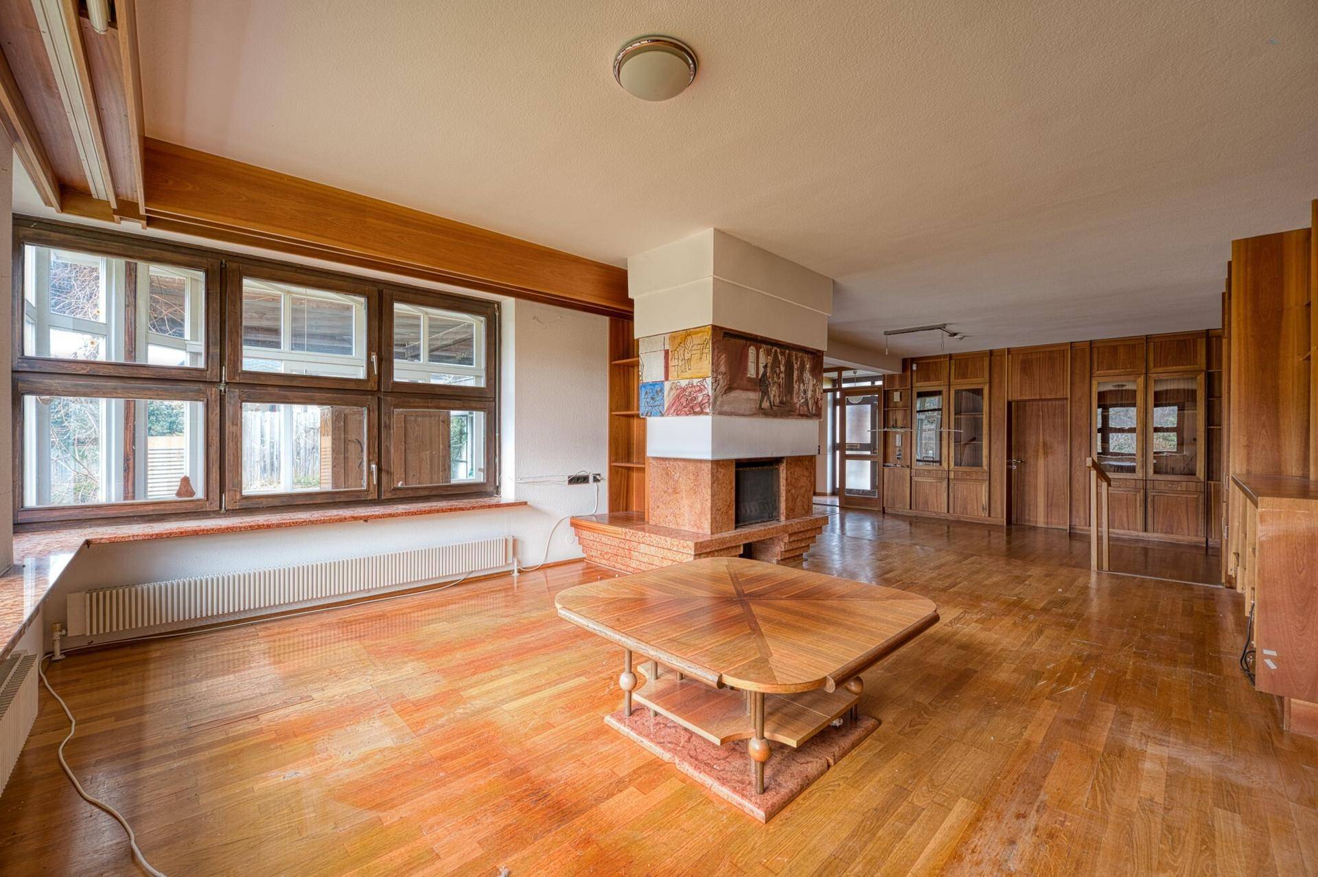 Heller Wohnbereich mit Holzboden, großen Fenstern und einem dekorativen Kamin.