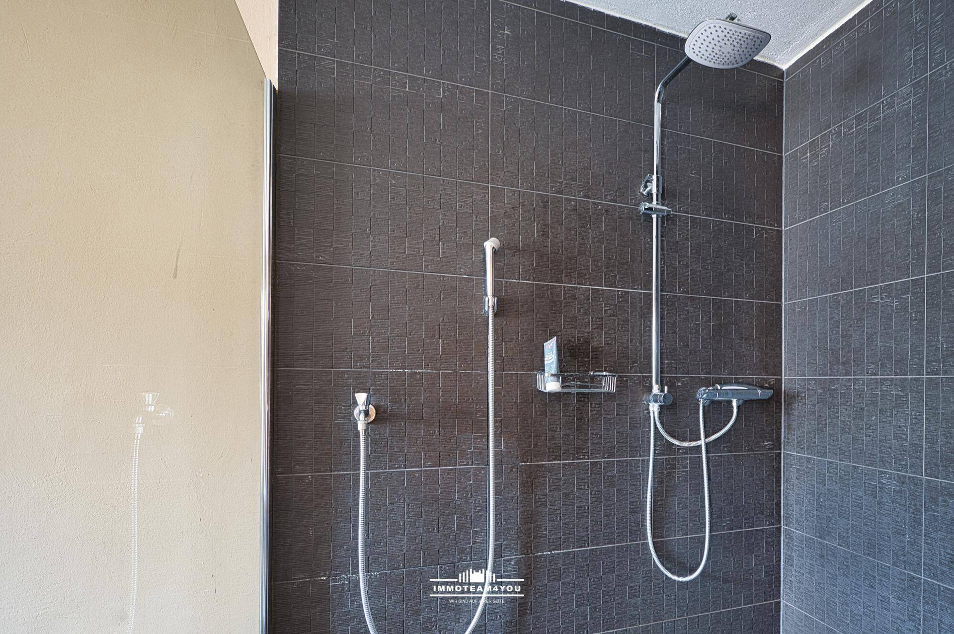 Moderne Dusche mit dunklen Fliesen und Regenduschkopf in einem Badezimmer.