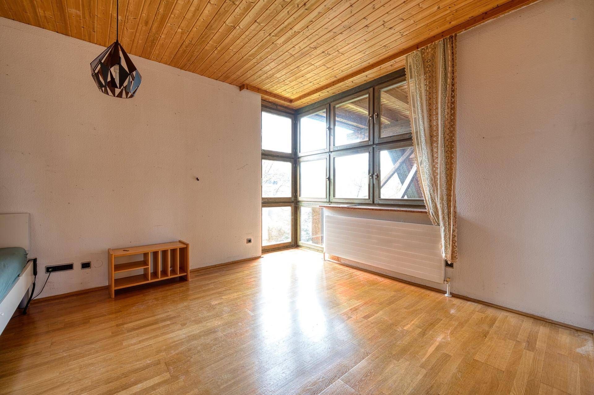 Helles Schlafzimmer im Dachgeschoss mit Holzboden, Holzdecke und großen Fenstern.