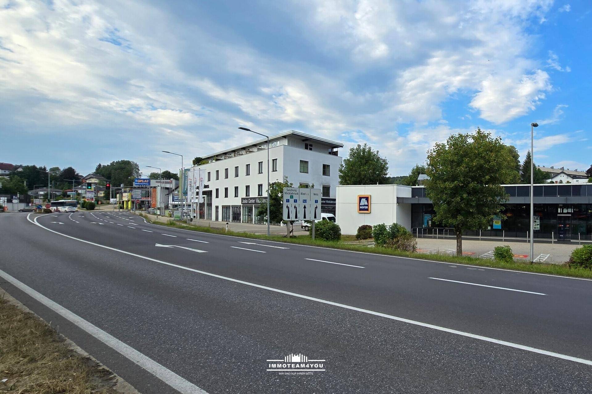 Weitläufige Ansicht der Geschäftsgebäude und der Straße, umgeben von Grünflächen unter bewölktem Himmel.