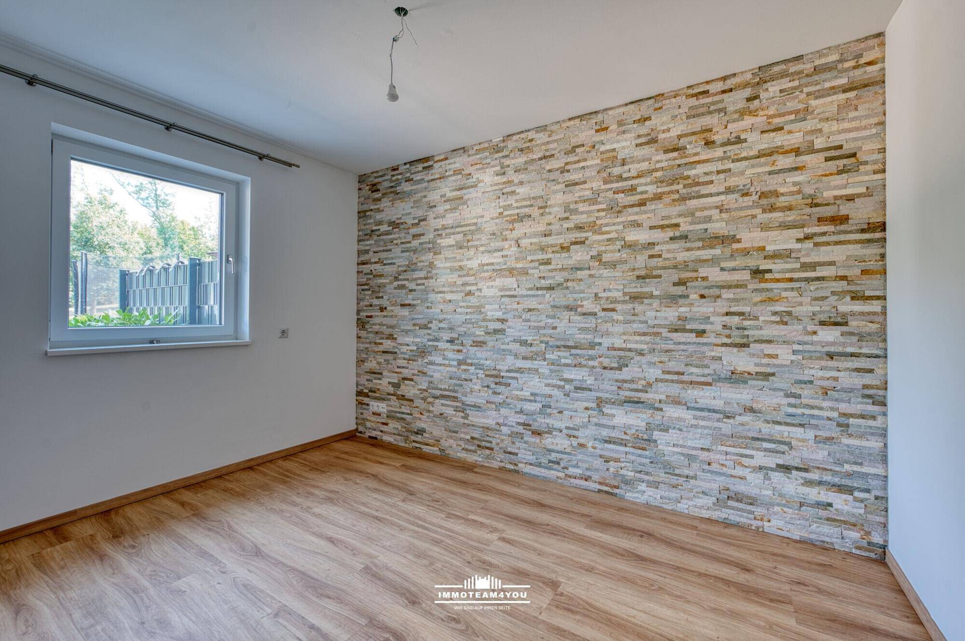 Helles Zimmer mit Laminatboden und einer dekorativen Steinwand.